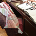 Handmade floral and hearts quilt shown draped over a chair at a desk