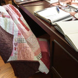 Handmade floral and hearts quilt shown draped over a chair at a desk