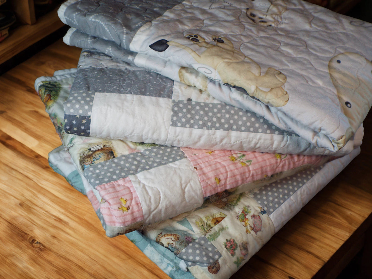 Folded baby quilts fanned out on a wooden shelf