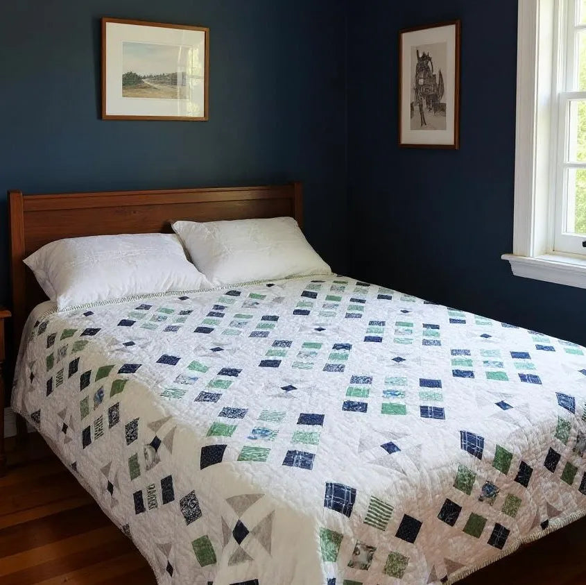 Handmade blue and green quilt shown in a dark minimally decorated room.
