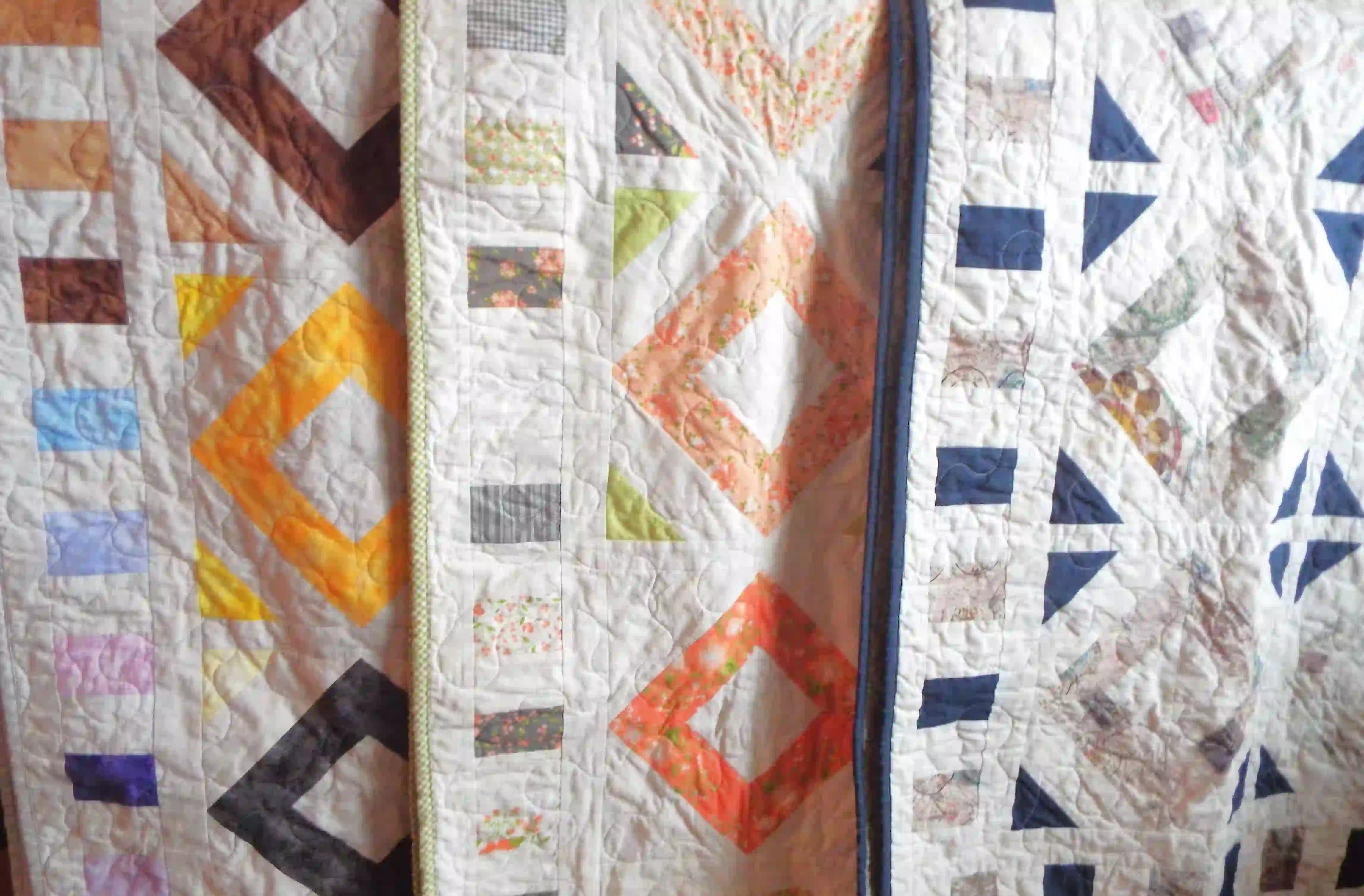 Three handmade quilts draped to show pattern, fabric, border, and binding. 