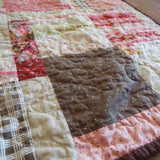 Stylized angled view of handmade floral and heart throw quilt with chocolate back