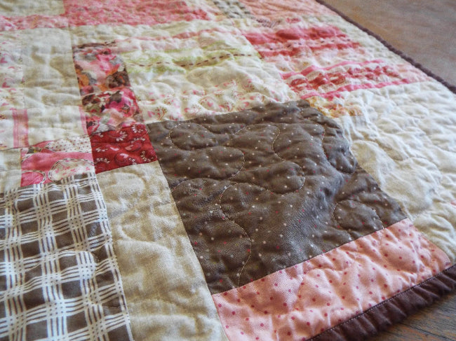 Stylized angled view of handmade floral and heart throw quilt with chocolate back
