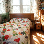 Bright red, green, and gray quilt shown in a small bedroom on a bed with a wooden headboard