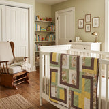 Honeyed Tails Baby Quilt shown draped over the side of a crib in a neutrally decorated nursery.