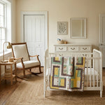 Honeyed Tails Baby Quilt shown draped over a crib in a minimally decorated nursery.