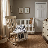Little Framework Baby Quilt shown on a rocking chair in a neutrally decorated nursery.