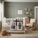 Little Framework Baby Quilt shown draped over a white crib in a soft green nursery.
