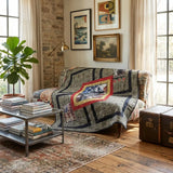 Marine Eagle Handmade Throw Quilt is draped over an armchair in a styled living room with a stone wall, windows, and a vintage trunk.