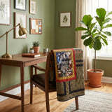 Marine Eagle Handmade Throw Quilt is draped over a wooden chair in a styled home office setting with a desk, lamp, and a large fiddle-leaf fig plant.