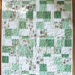 Full top-down view of handmade green and soft white baby quilt with whimsical bunny fabric