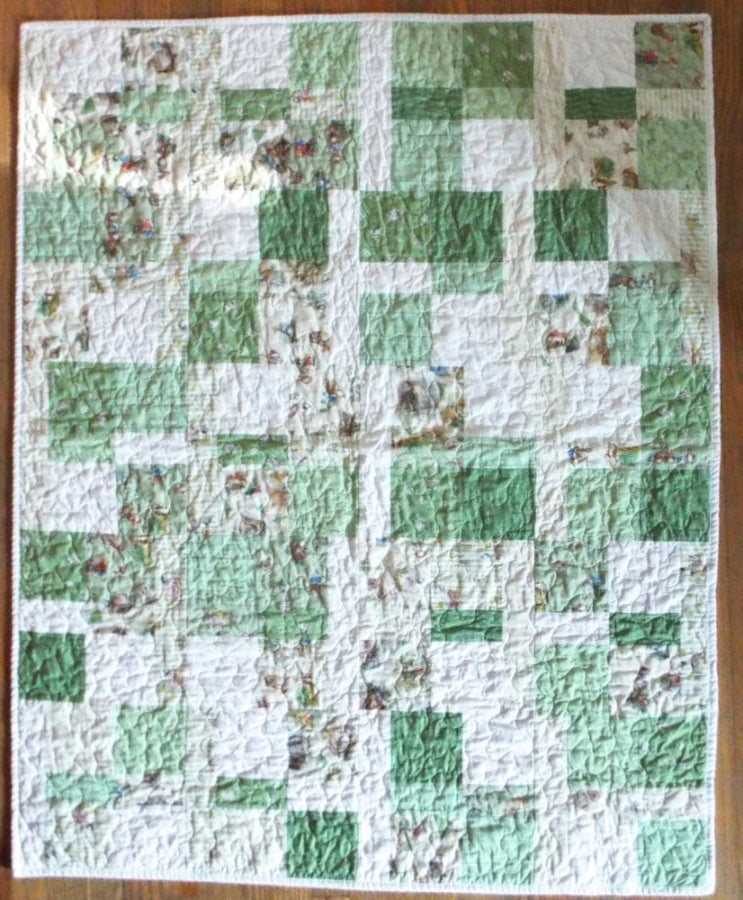 Full top-down view of handmade green and soft white baby quilt with whimsical bunny fabric