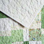 Corner flip of green baby quilt showing tone-on-tone white cotton backing and character patchwork