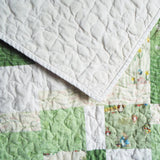 Corner flip of green baby quilt showing tone-on-tone white cotton backing and character patchwork