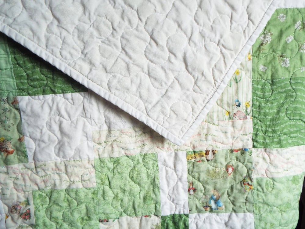 Corner flip of green baby quilt showing tone-on-tone white cotton backing and character patchwork