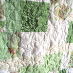 Close-up of handmade green baby quilt showing free-motion stitching and storybook character prints
