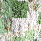 Close-up of handmade green baby quilt showing free-motion stitching and storybook character prints