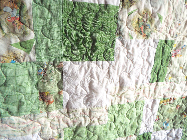 Close-up of handmade green baby quilt showing free-motion stitching and storybook character prints