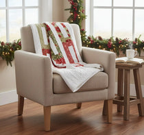 Neutral armchair with holiday quilt draped over it in the corner of an airy room