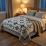 Quilt shown on a wooden bed in a minimally styled room with bedside lamp on.
