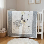 Handmade gray and white safari animal baby quilt hanging on white crib in softly lit nursery