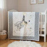 Handmade gray and white safari animal baby quilt hanging on white crib in softly lit nursery