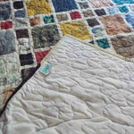 Corner of the Of Ink and Thread King Quilt folded to reveal the soft neutral backing, signature SQ² label, and free-motion quilting pattern.