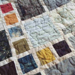 Close-up of fabric blocks featuring script, maps, and vintage-inspired designs stitched together in balanced geometric layout.