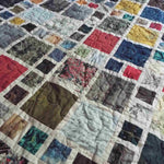 Close view of the Of Ink and Thread King Quilt showing its mosaic-style patchwork in rich blues, greens, reds, and map-inspired prints.