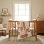 Baby quilt hanging over a wooden crib in a classic neutral nursery with a rocking chair and woodland artwork, emphasizing the quilt’s heirloom-inspired patchwork.