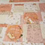 Close-up of the quilt’s center blocks showing detailed hare illustrations, soft peach tones, and gentle meandering quilting stitches.