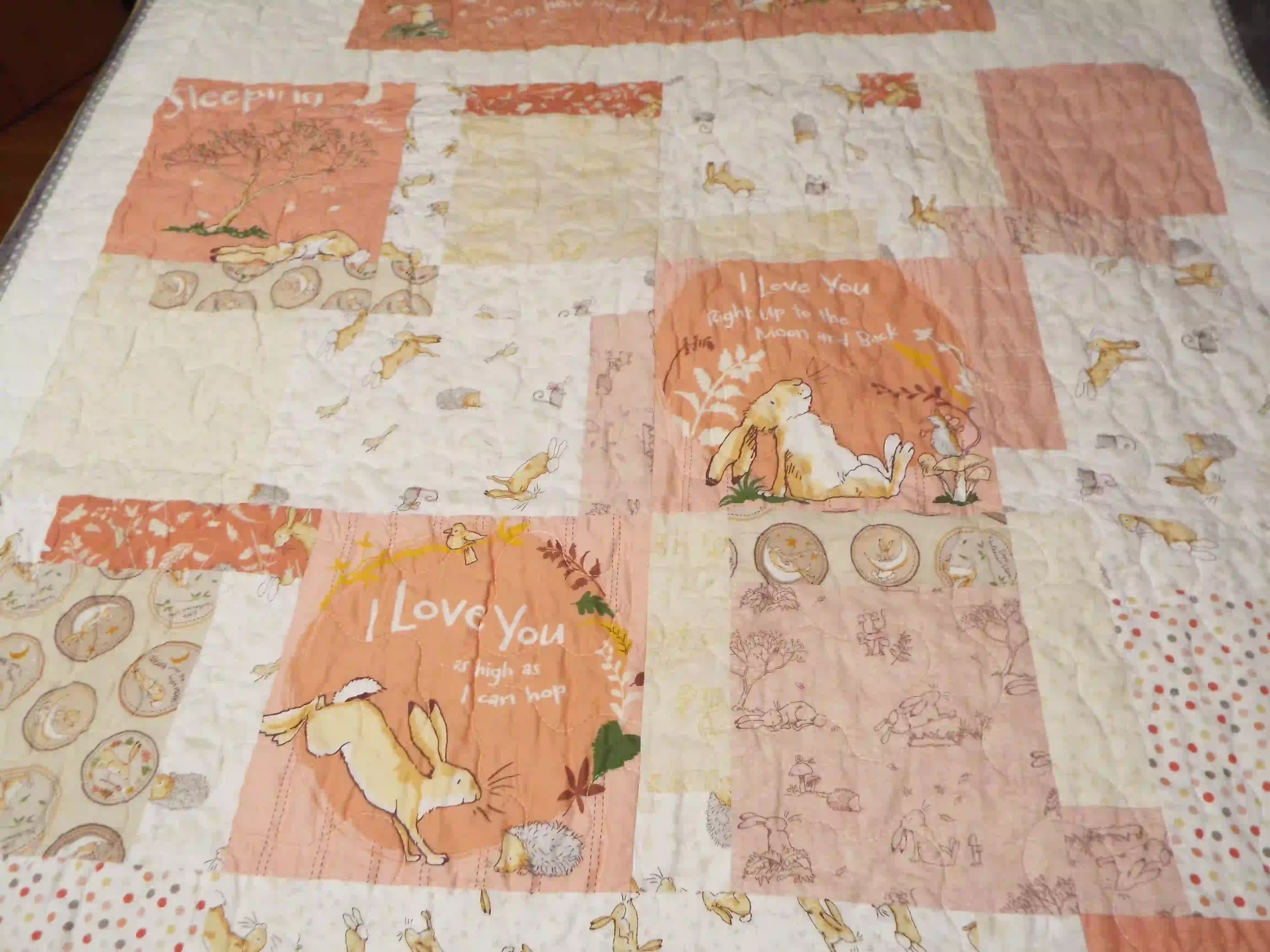 Close-up of the quilt’s center blocks showing detailed hare illustrations, soft peach tones, and gentle meandering quilting stitches.