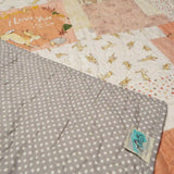 Corner of the quilt flipped back to reveal the gray polka-dot backing and handmade label, highlighting craftsmanship, stitching, and finish.