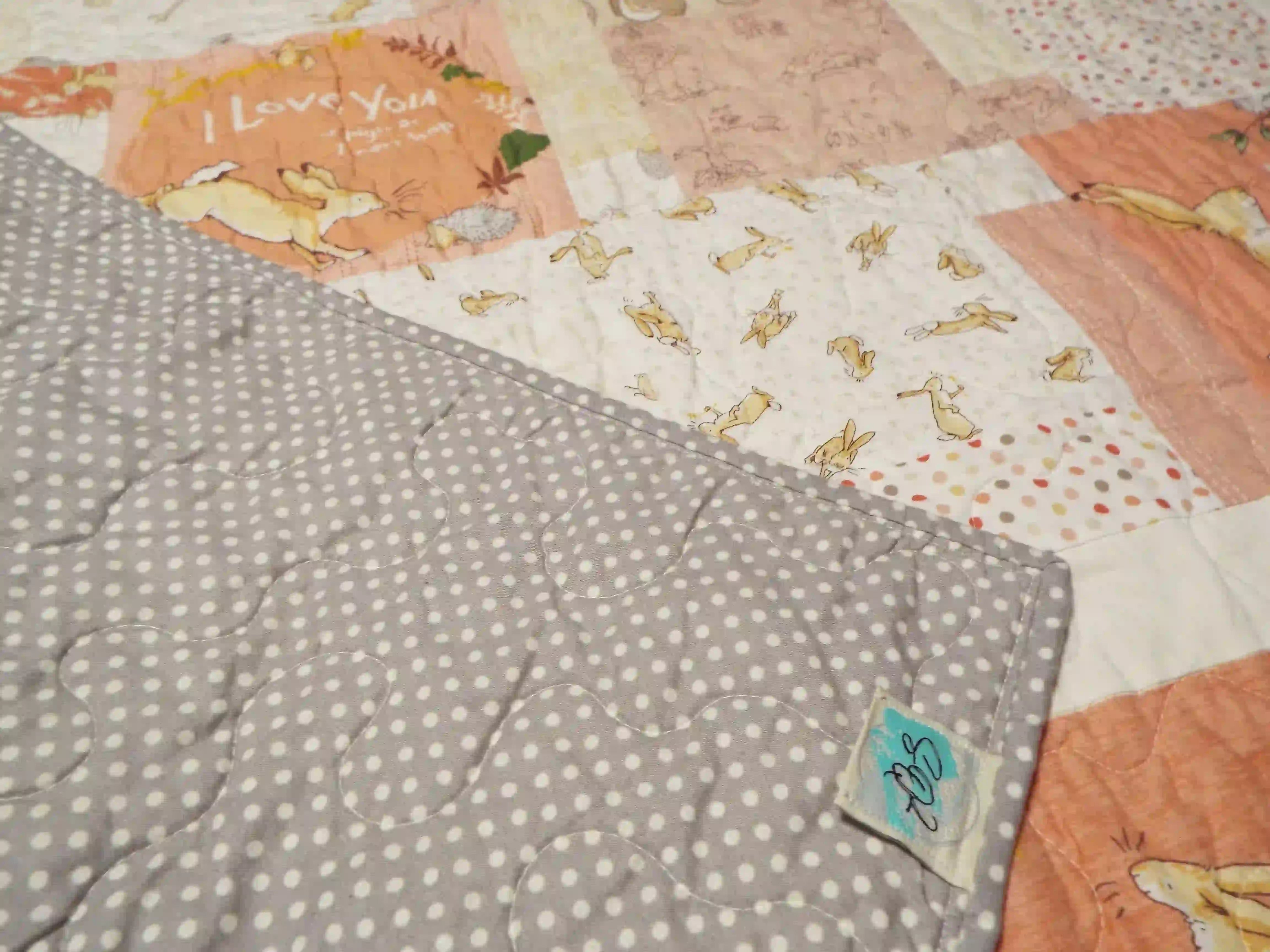 Corner of the quilt flipped back to reveal the gray polka-dot backing and handmade label, highlighting craftsmanship, stitching, and finish.