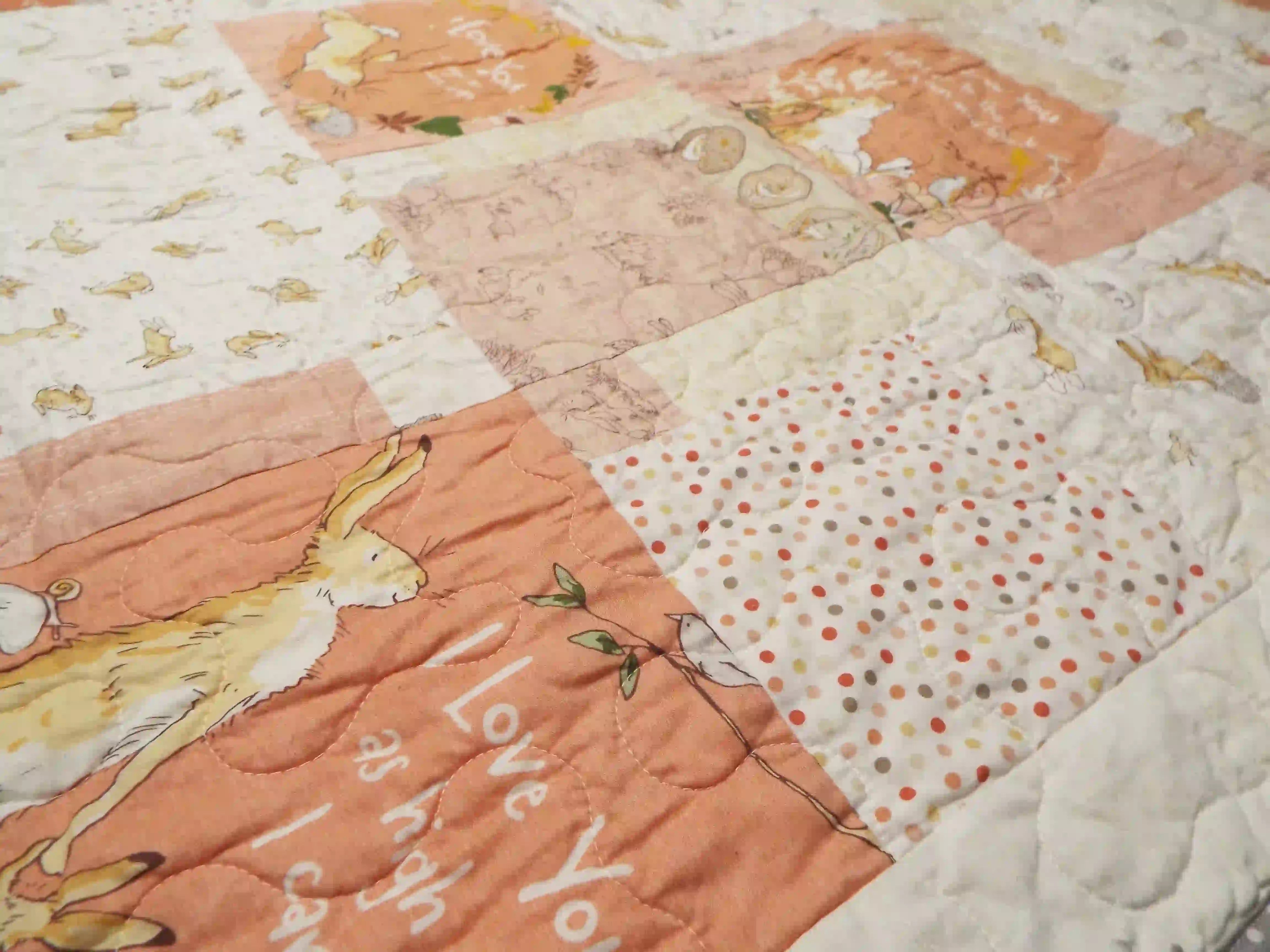 Angled detail shot of the baby quilt’s patchwork sections, showing fabric textures, soft color transitions, and the delicate quilting pattern.