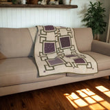 Handmade purple and cream throw quilt draped over a neutral sofa with modern farmhouse décor and a potted plant in the background.