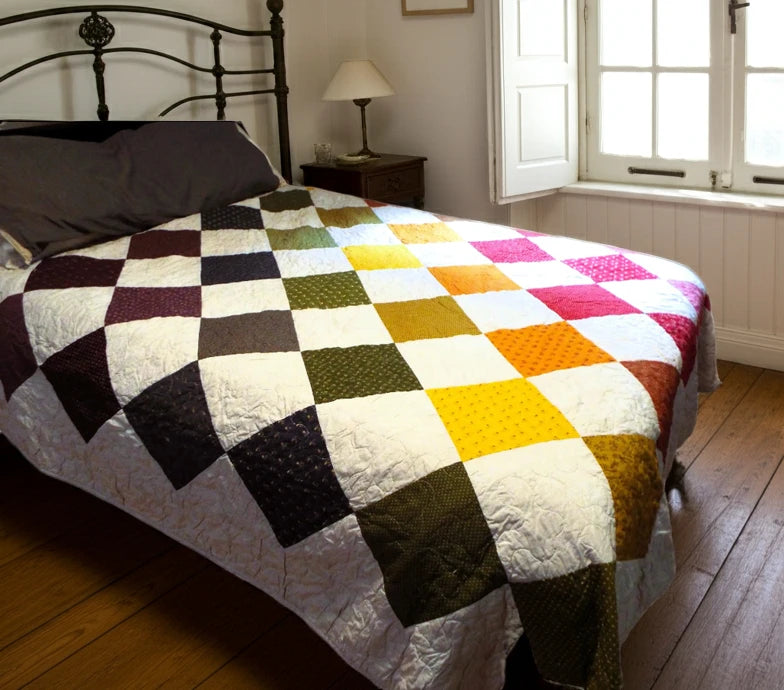 Handmade rainbow patchwork quilt on queen bed with iron headboard and soft morning light through window