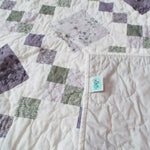 Quiet Meadow shown with corner flipped over to display backing, quilt stitching detail, and tag.