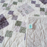 Quiet Meadow shown with corner flipped over to display backing, quilt stitching detail, and tag.