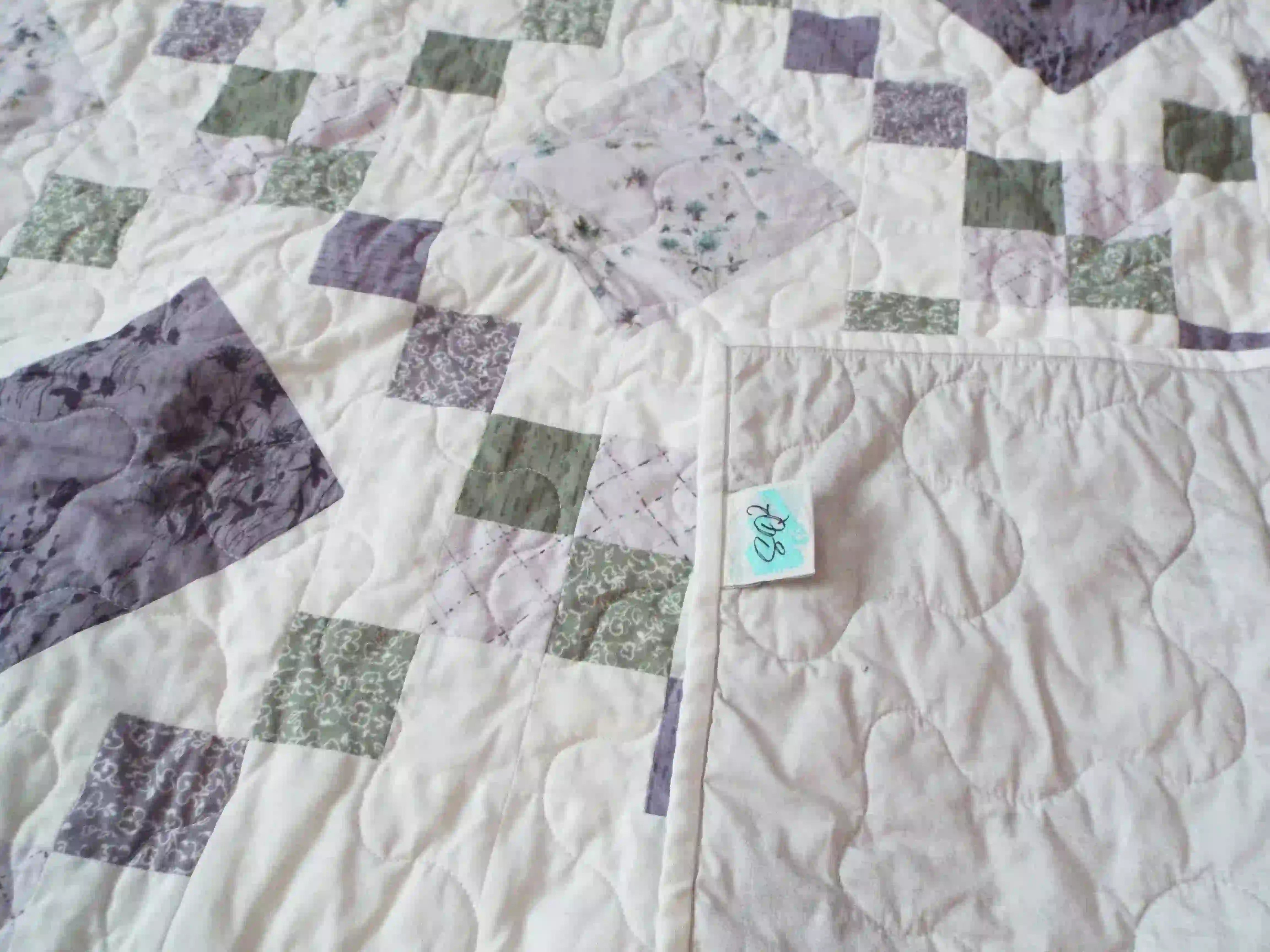 Quiet Meadow shown with corner flipped over to display backing, quilt stitching detail, and tag.