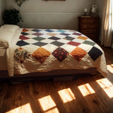 Close-up of handmade patchwork quilt featuring gold, plum, and forest green floral prints.