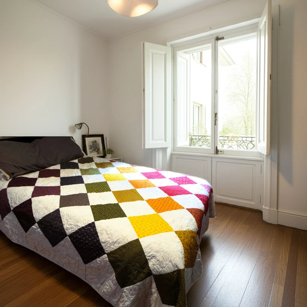 Handmade rainbow quilt on queen bed in bright minimalist bedroom with white walls and open window