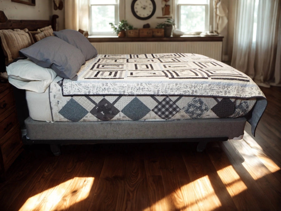 Black and white modern quilt with geometric patchwork draped over a bed in a rustic farmhouse bedroom setting.