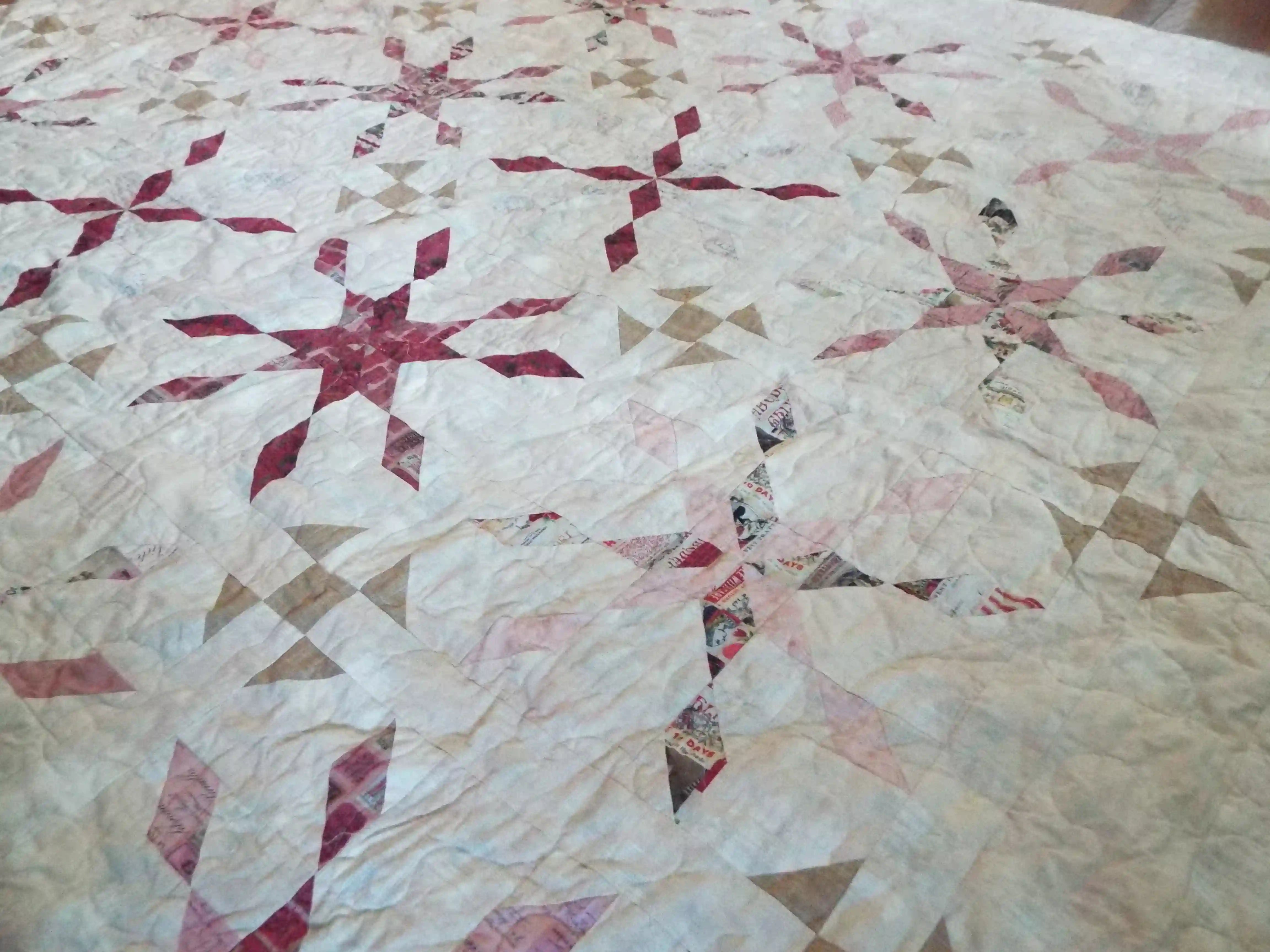 Angled lay of Scarlet Correspondence Queen Quilt showing more detail of design and stitching.