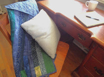 Blue quilt shown draped over a chair with a pillow in the chair pulled out from a desk