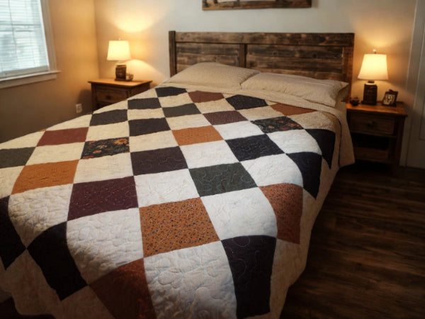 Handmade queen quilt with floral patchwork in autumn tones on a cozy wood-floor bedroom bed.