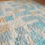 Angled view of handcrafted blue and cream baby quilt with whimsical bunny patterns