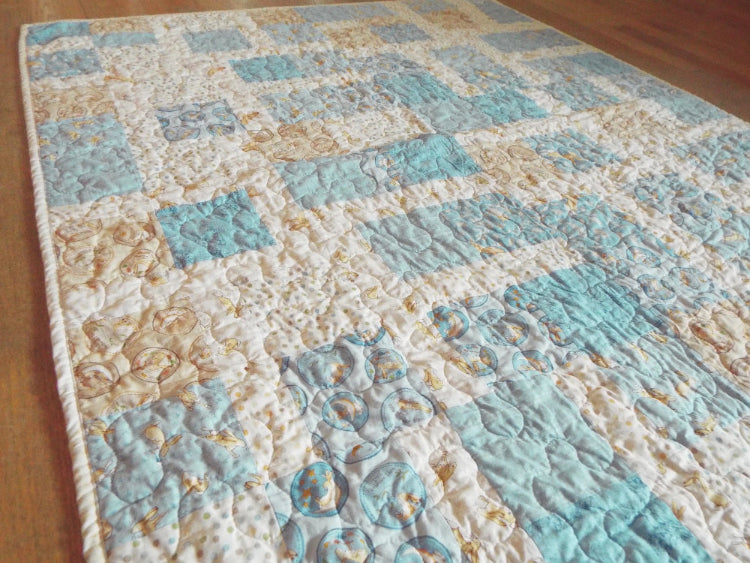 Angled view of handcrafted blue and cream baby quilt with whimsical bunny patterns
