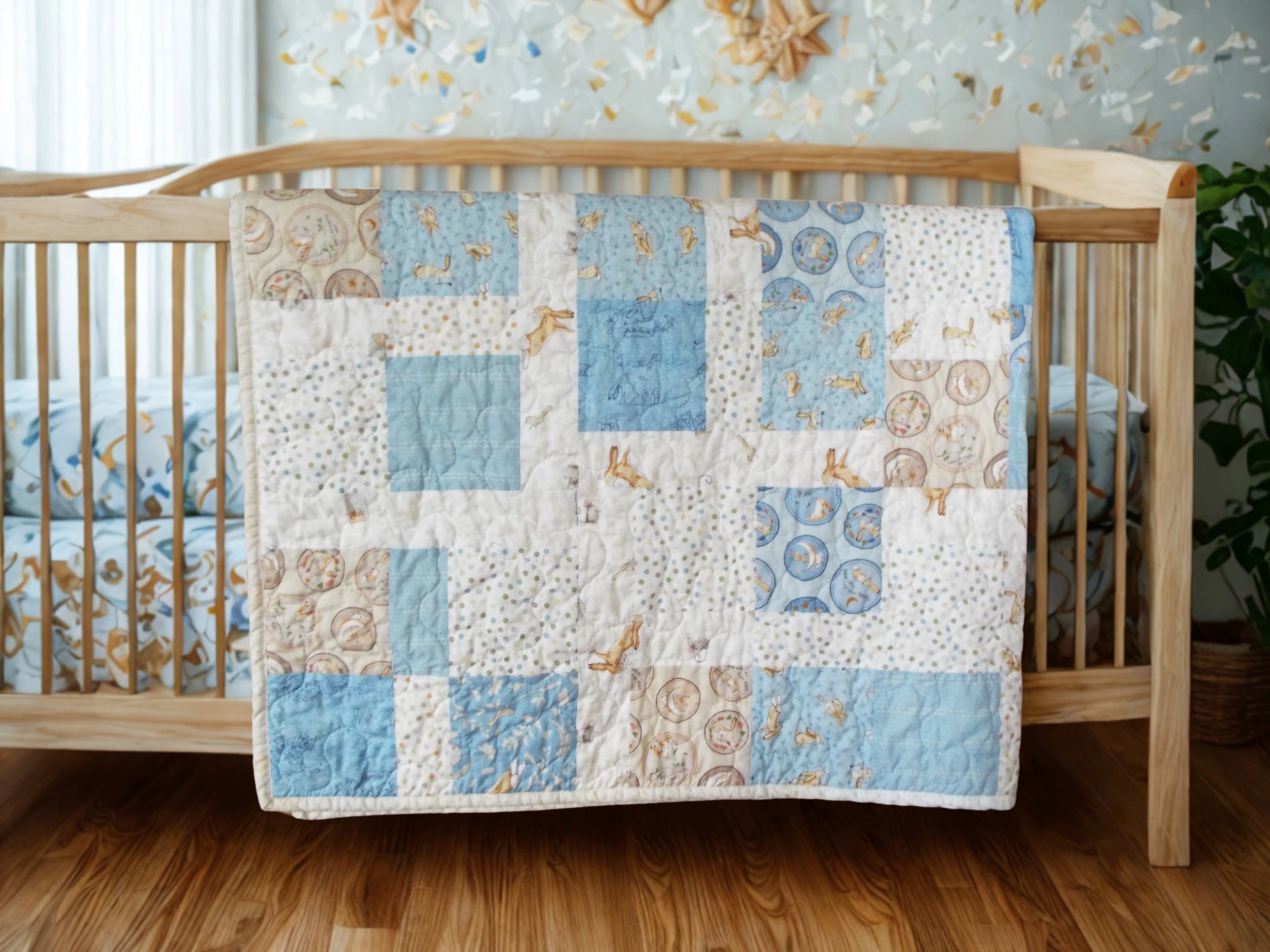 Handmade blue baby quilt draped over wooden crib in nursery with wood floors