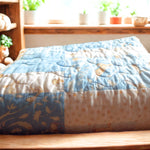 Folded blue baby quilt with bunny and polka-dot prints on nursery shel with soft toys